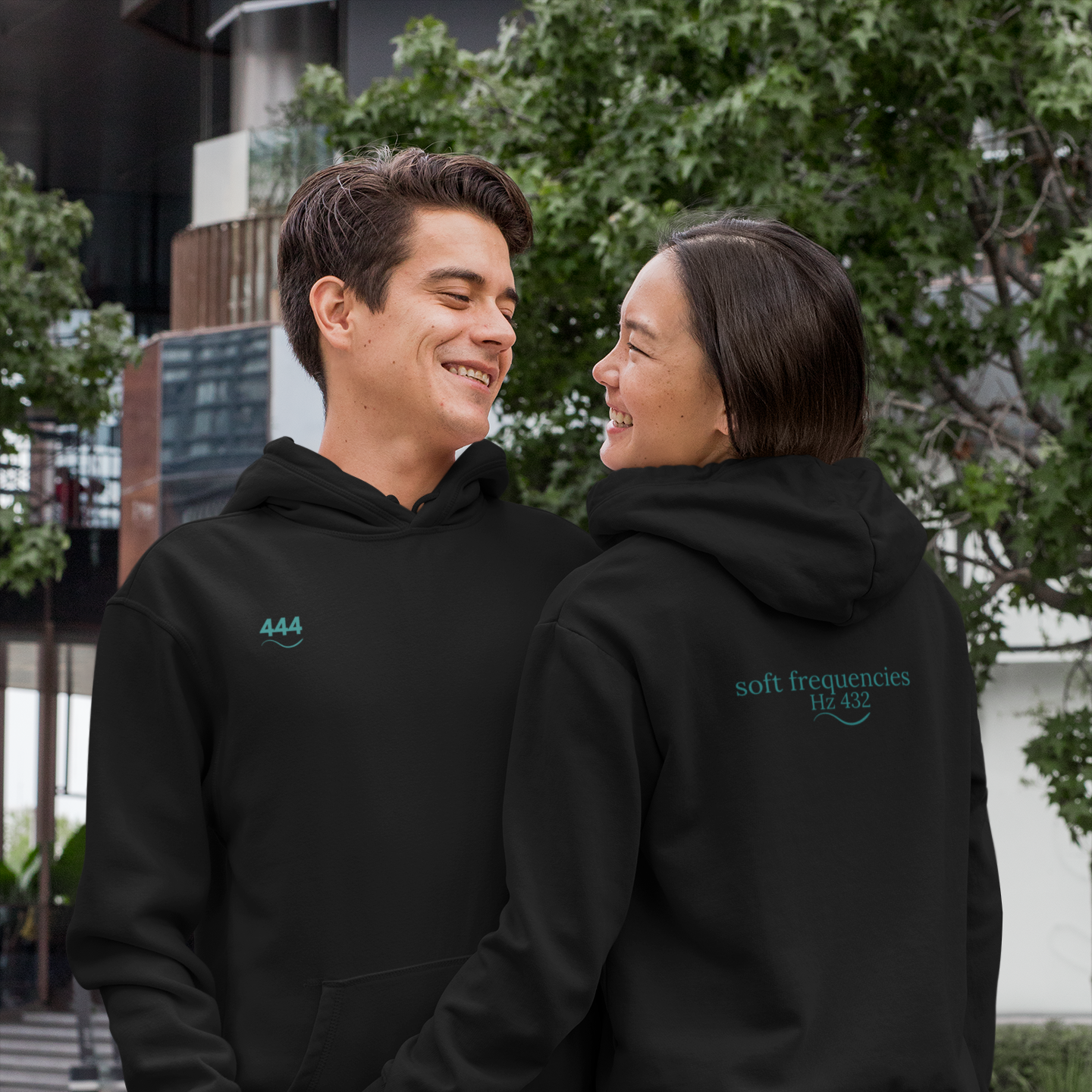 Couple wearing Soft Frequencies 444 Eclipse Hoodies, featuring angel number print on front and Hz 432 frequencywear logo on back in teal on black fleece